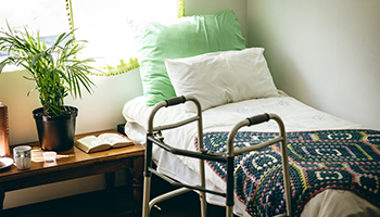 Front view of empty bed and walker in bed room at retirement home